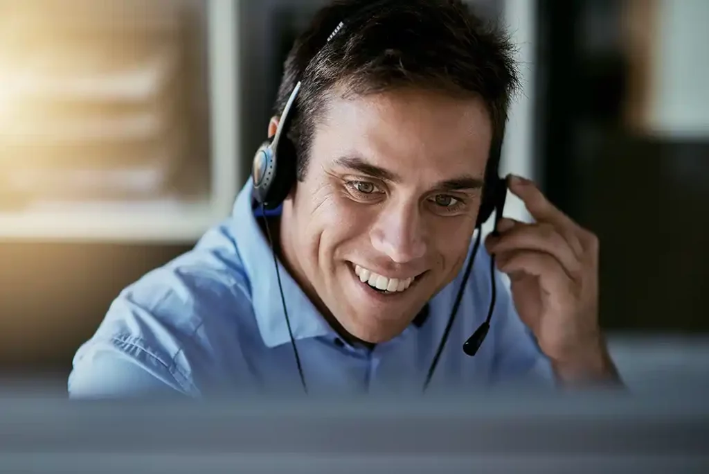 Brunhårig leende support kille i blå skjorta och headset hjälper kunder med deras frågor.